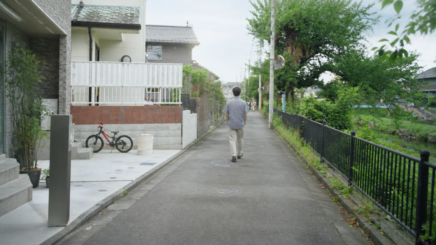 住宅街の家から離れて歩く充を表した後ろ姿